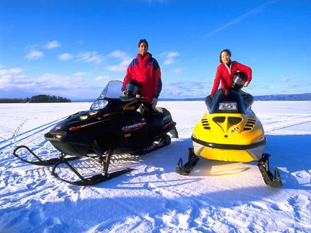 Two people on two snowmobiles on a frozen lake at Algonquin Park