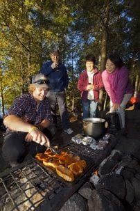 Guests standing around a bon fire while the Voyageur Quest guide is preparing their dinner