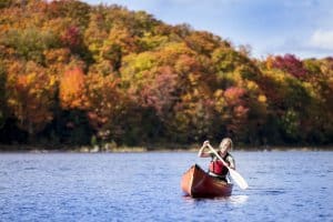 A person canoeing in a red canoe and in the background Algonquin Autumn colours