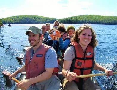 Group of guests in a big canoe paddling on a lake at Algonquin Park during a 3 day Log Cabin adventure
