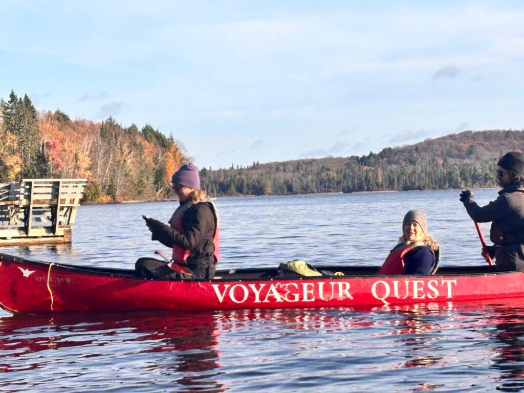 Guests paddling a red Voyageur Quest canoe on an Algonquin lake with fall colours on the hills
