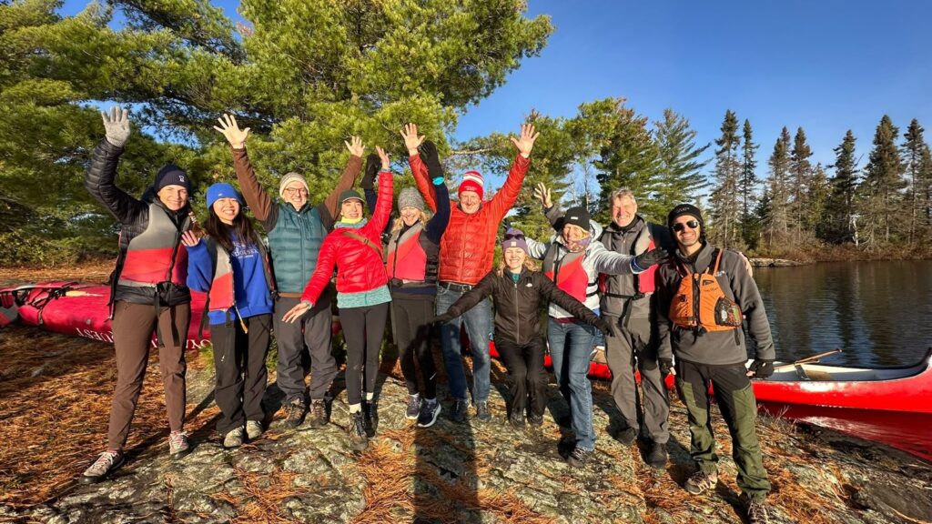 Fall Wellness group waving on a rocky shore beside red canoes in Algonquin Park