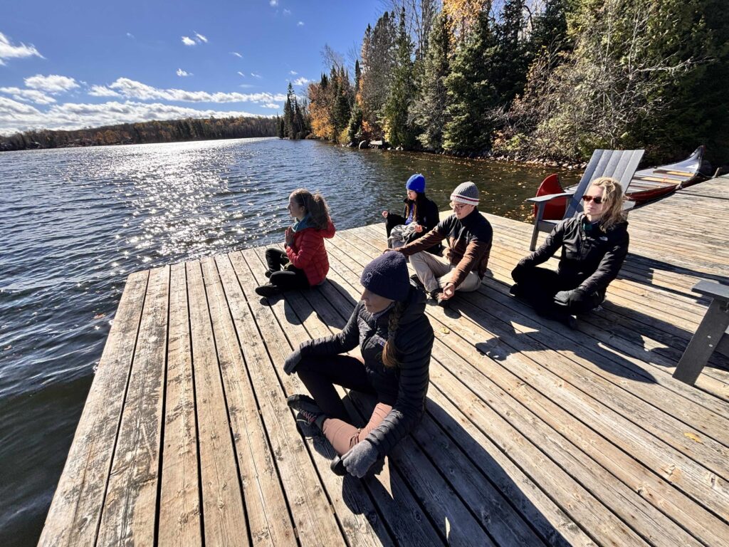 Guests doing breathwork on a dock overlooking an Algonquin lake in fall